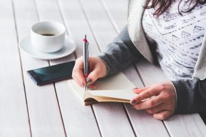 Women planning workout routine in notebook and tracking on mobile for fitness
